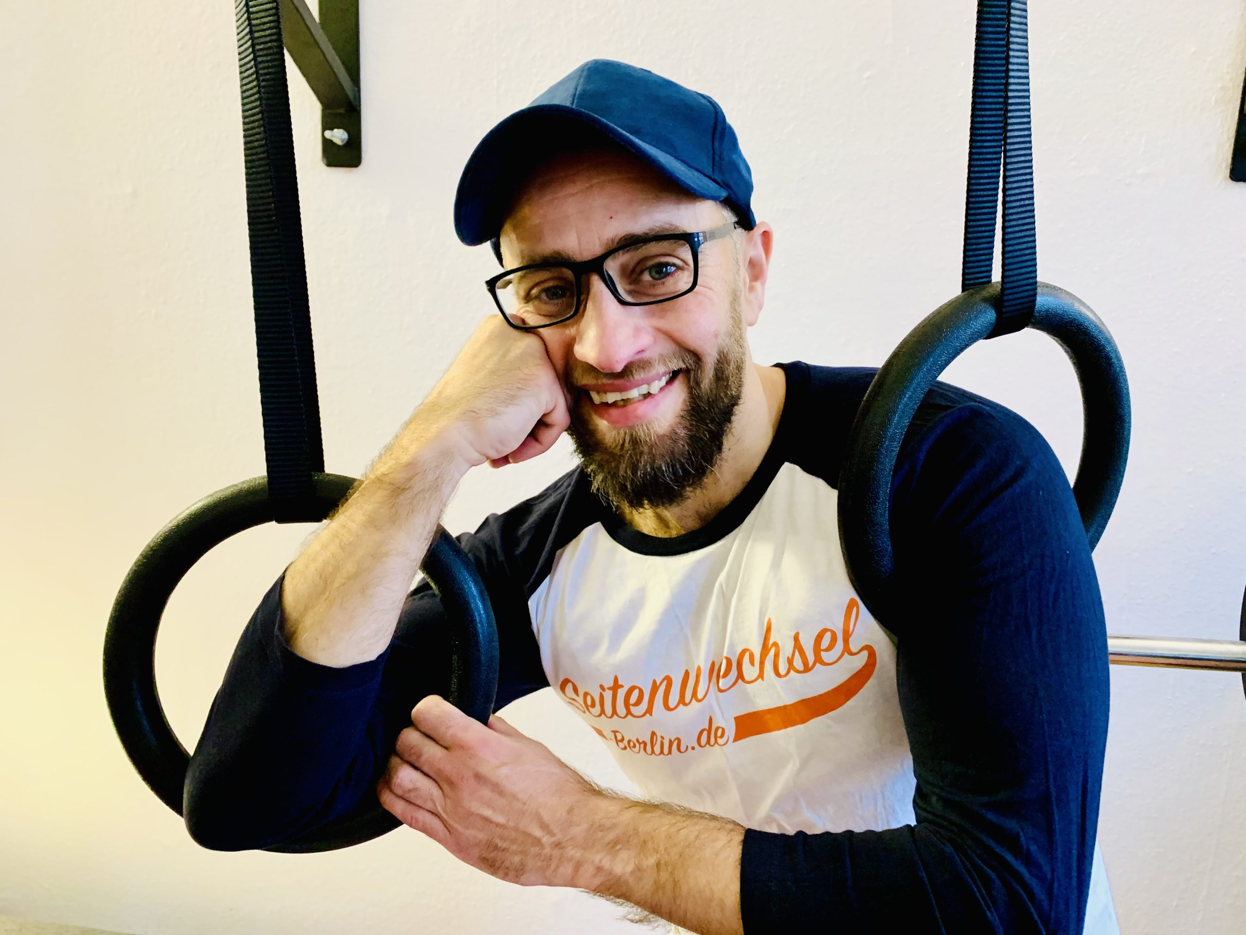 Person wearing glasses and a baseball cap next to a couple of workout rings